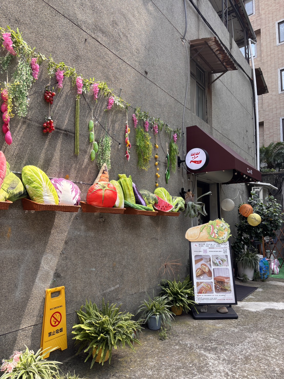 芝山棧台北士林店外觀，牆面掛滿蔬菜造型裝飾與彩色植栽，門口立有菜單看板